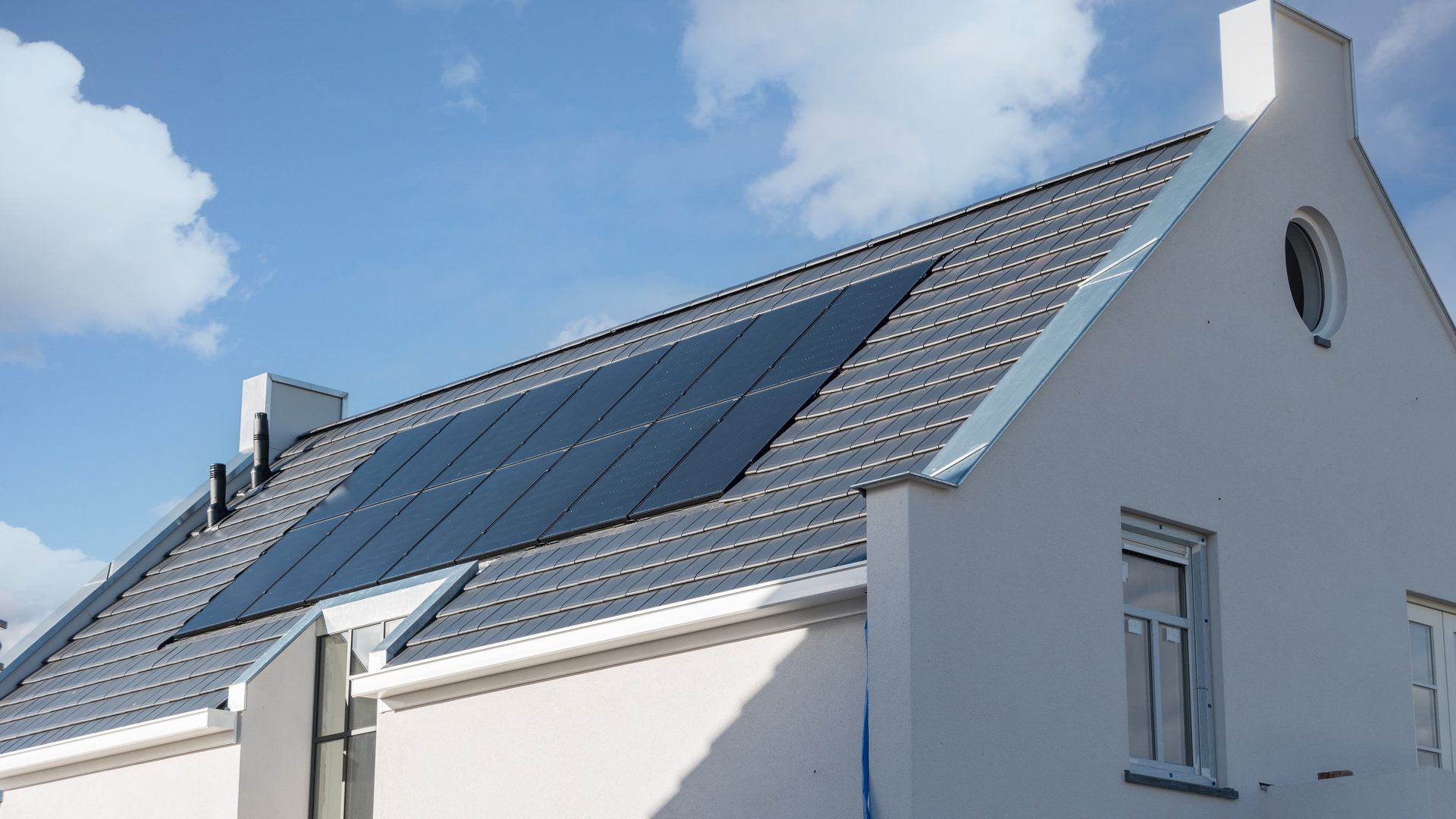 Modern white gabled home with solar panels under a wide blue sky